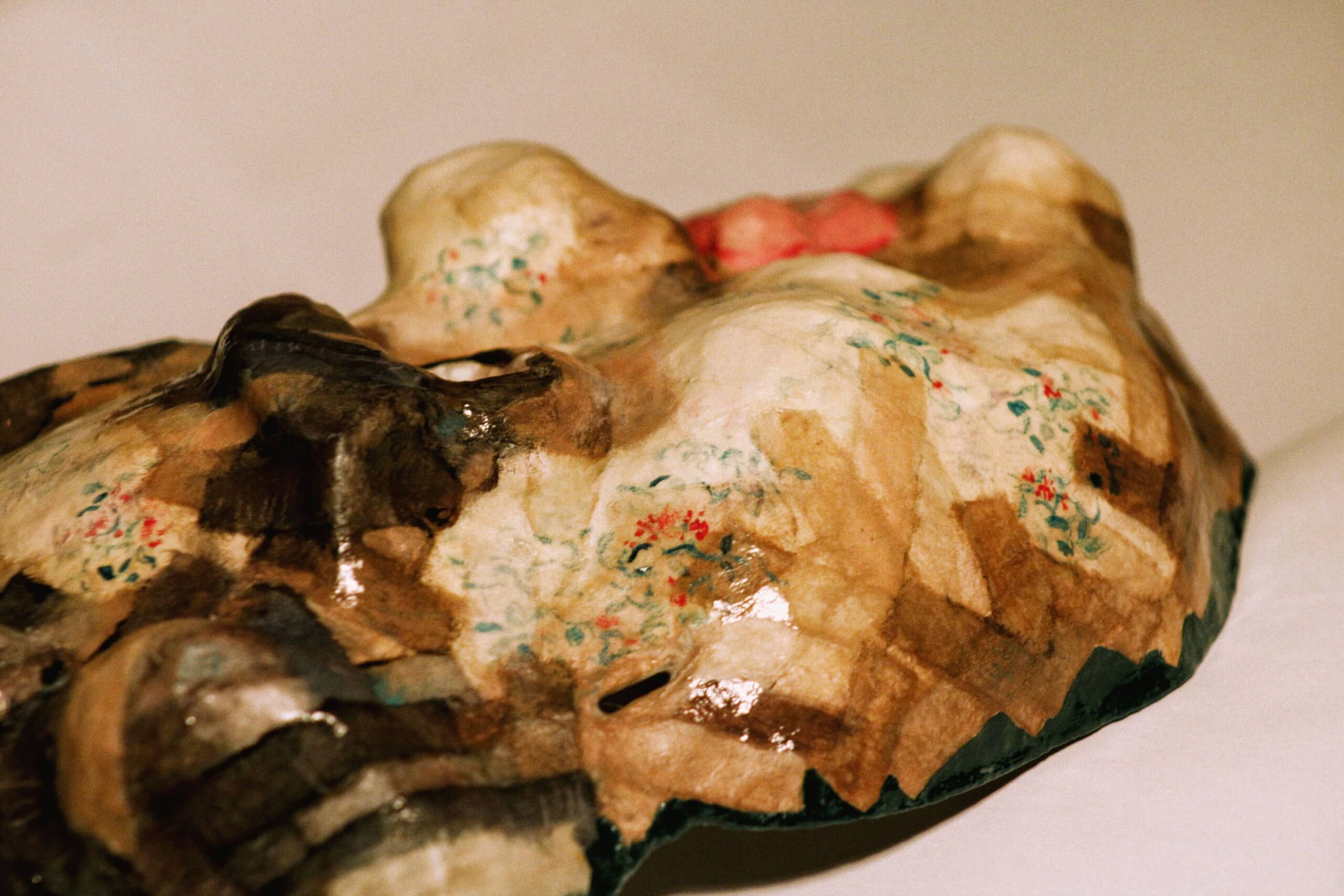detail of a sculpted cheek with painted vine-like flowers, layered over brown paper and glistening varnish