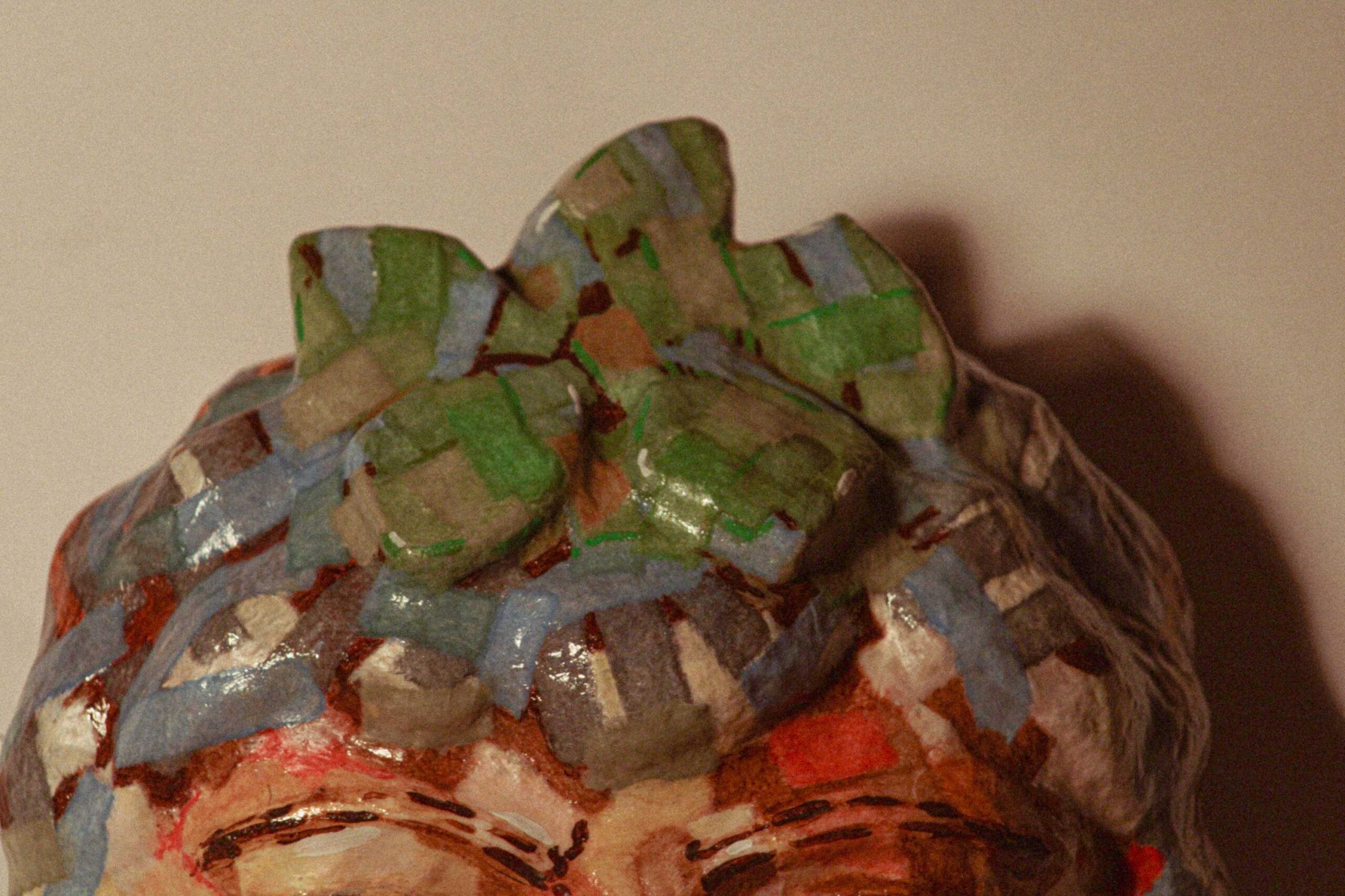 close-up of the top of the sculpted head, featuring raised, rounded forms painted in green and blue tones, resembling stylized hair